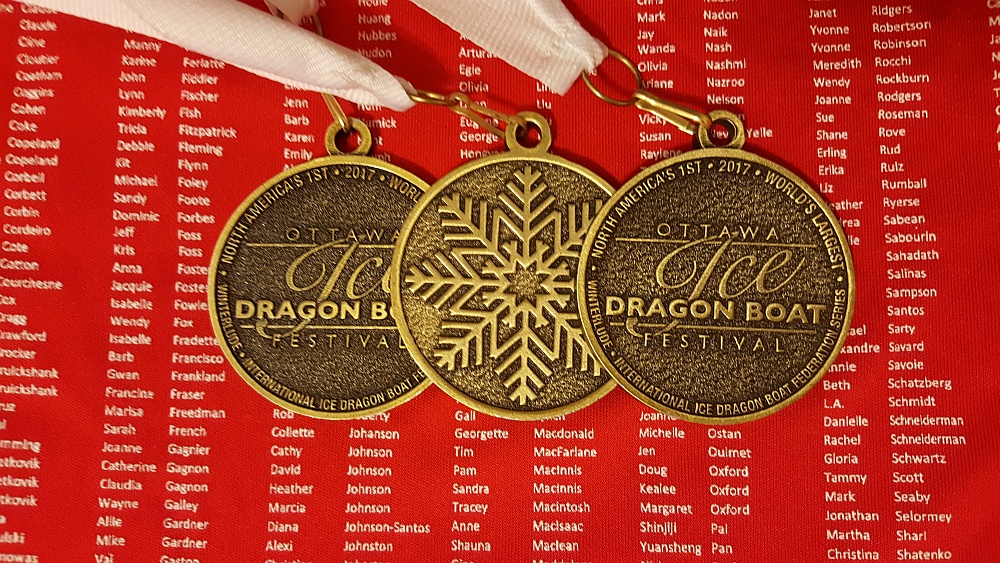 Picture of three of the participation medals from the event, with background being red souvenir jersey that has every participant's name on it.
